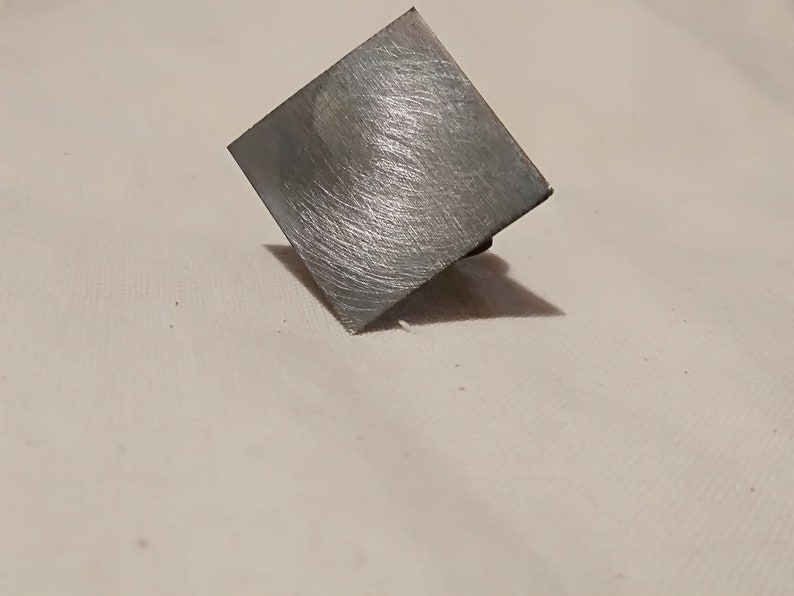 May include: A silver square-shaped metal object with a brushed finish.