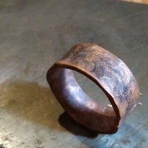 May include: A wide copper band ring with a hammered finish. The ring has a rustic, aged look.