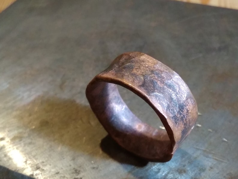 May include: A wide copper band ring with a hammered finish. The ring has a rustic, aged look.
