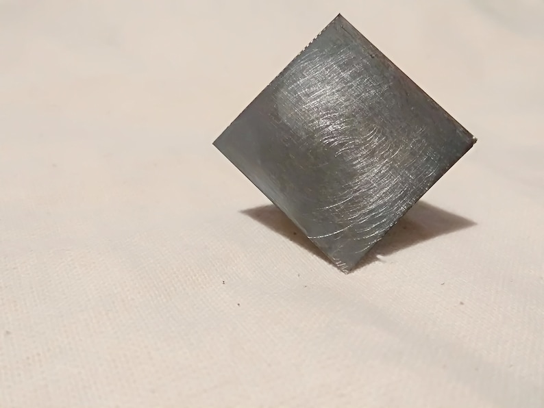 May include: A square piece of metal with a brushed finish. The metal is a light gray color.