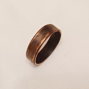 May include: A copper ring with a brushed finish. The ring has a wide band and a slightly rounded edge.