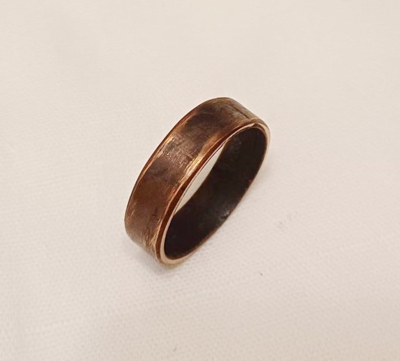 May include: A copper ring with a brushed finish. The ring has a wide band and a slightly rounded edge.