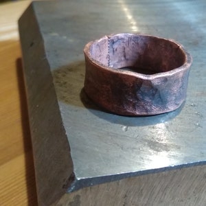 May include: A hammered copper ring with a rough, textured surface. The ring is a warm, reddish-brown colour and has a slightly irregular shape.