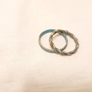 May include: Two gold-toned rings with a blue enamel finish. The rings are intertwined and have a twisted design.