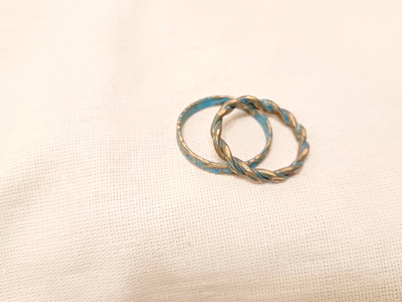 May include: Two gold-toned rings with a blue enamel finish. The rings are intertwined and have a twisted design.