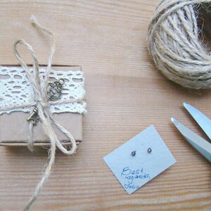 Puede incluir: Una peque&ntilde;a caja marr&oacute;n envuelta con cuerda y encaje, atada con un dije de llave. La caja est&aacute; sobre una superficie de madera junto a una tarjeta con el texto "Saludos cordiales, Julia".
