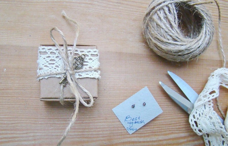 Puede incluir: Una peque&ntilde;a caja marr&oacute;n envuelta con cuerda y encaje, atada con un dije de llave. La caja est&aacute; sobre una superficie de madera junto a una tarjeta con el texto "Saludos cordiales, Julia".