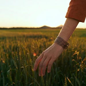 Op de afbeelding: Een stapel dunne, donker metalen armbanden gedragen om de pols. De armbanden hebben een getextureerd, gehamerd oppervlak en een diepe, gebruinde afwerking. De set bestaat uit meerdere individuele ringen die dicht op elkaar zitten.