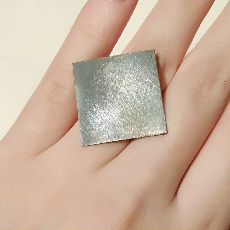 May include: A silver square ring with a brushed finish.