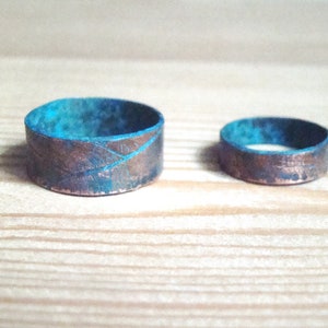 May include: Two copper rings with a turquoise patina. The larger ring has a textured surface.