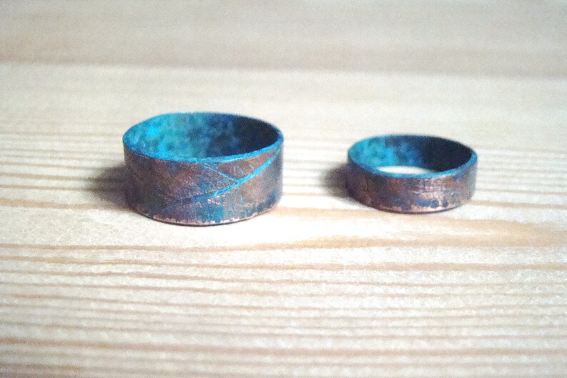 May include: Two copper rings with a turquoise patina. The larger ring has a textured surface.