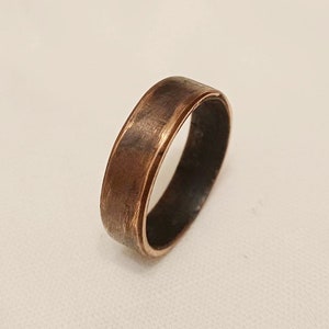 May include: A wide copper band ring with a smooth, slightly textured finish. The ring has a beveled edge and a slightly darker inner band.