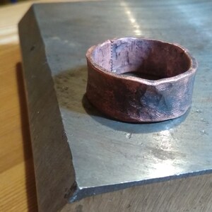 May include: A wide copper ring with a hammered finish. The ring has a rough, textured surface and is slightly oxidised.