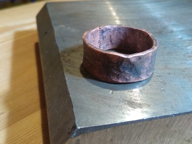 May include: A wide copper ring with a hammered finish. The ring has a rough, textured surface and is slightly oxidised.