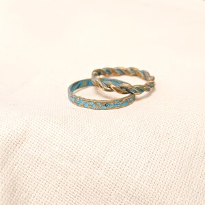 May include: Two gold rings with a blue speckled finish. The ring on top is a twisted band.