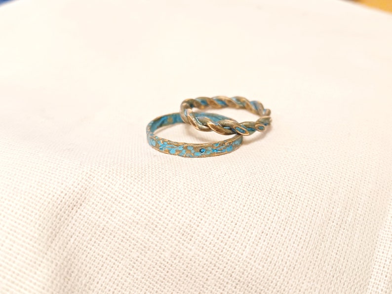 May include: Two gold rings with a blue speckled finish. The ring on top is a twisted band.