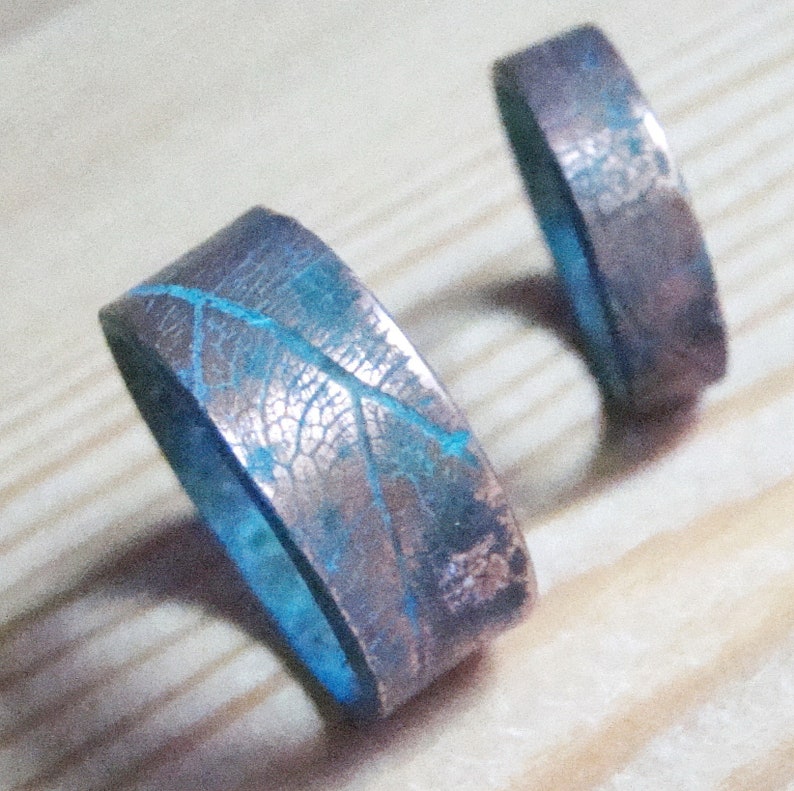 May include: Two copper rings with a blue leaf design. The rings are stacked on top of each other.