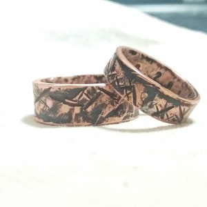 Puede incluir: Dos anillos de cobre con un dise&ntilde;o texturizado y estampado. Los anillos est&aacute;n apilados uno encima del otro.