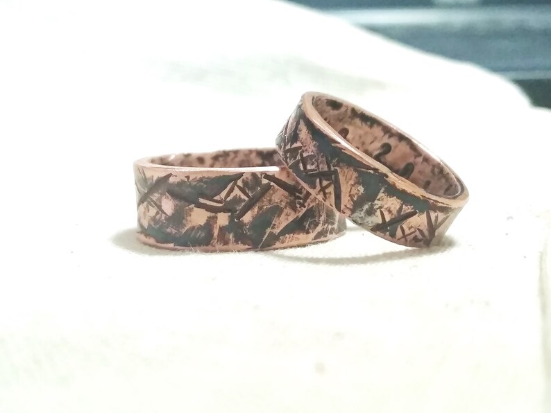 Puede incluir: Dos anillos de cobre con un dise&ntilde;o texturizado y estampado. Los anillos est&aacute;n apilados uno encima del otro.