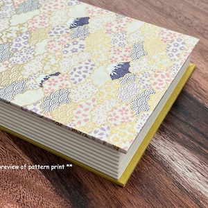 Puede incluir: Un libro blanco con un patrón floral dorado y rosa en la portada. El libro está cerrado y la encuadernación es visible. El libro está sobre una superficie de madera.