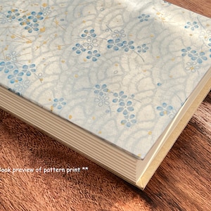 Puede incluir: Un libro con una cubierta azul claro que presenta un delicado patrón floral en tonos azules y dorados. El libro está cerrado y la encuadernación es visible.