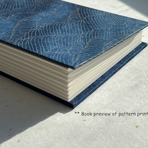 Puede incluir: Un libro azul con un patrón de ondas en la portada. El libro está cerrado y la encuadernación es visible. El libro está sobre una superficie blanca.