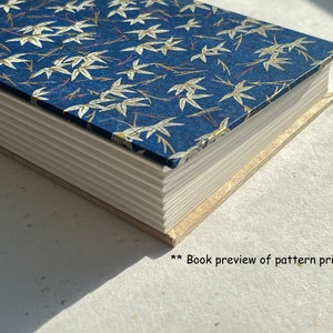 Puede incluir: Un libro azul con un patrón de bambú blanco y dorado en la portada. El libro está cerrado y la encuadernación es visible.
