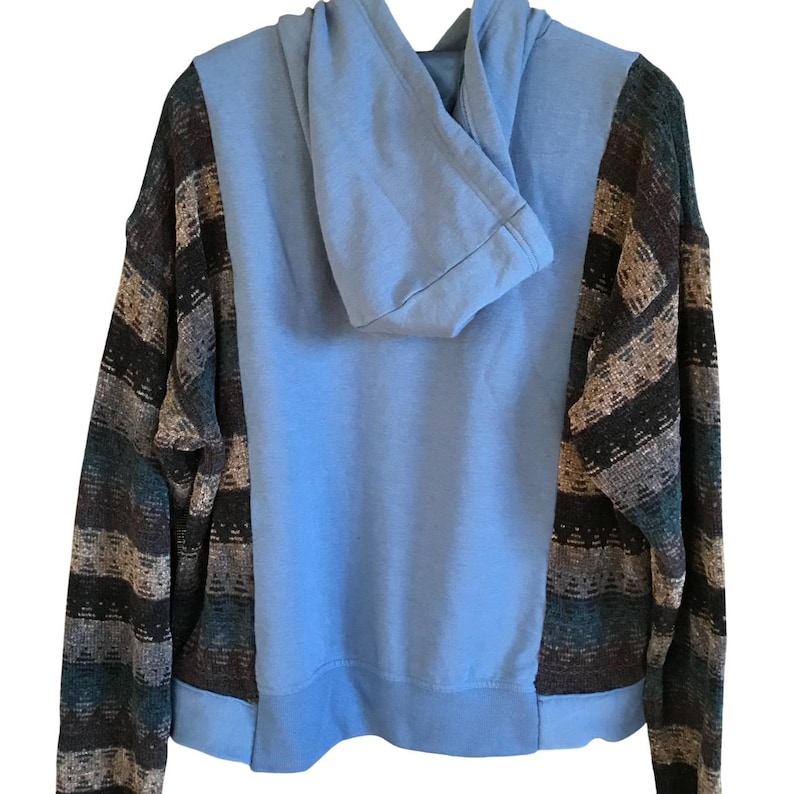 May include: A long-sleeve hoodie featuring a solid light blue center panel and hood, contrasted by sleeves and side panels with a multi-colored horizontal striped pattern in shades of dark brown, tan, black, and muted teal blue.
