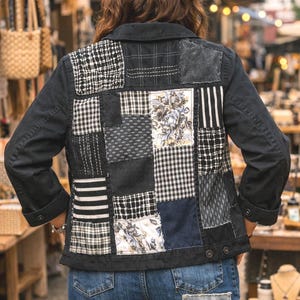 May include: Black denim jacket with a patchwork design on the back. The patches feature various patterns in black, white, and gray, including floral prints, stripes, and checks. The jacket is paired with blue jeans.