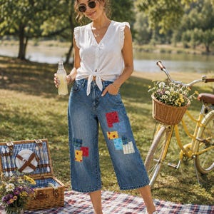 May include: A white sleeveless blouse with a V-neckline and a front tie closure, paired with blue denim cropped jeans featuring various colorful fabric patches in red, blue, and yellow patterns, worn with white canvas low-top sneakers.