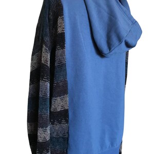 May include: A hooded sweatshirt featuring a solid light blue back and hood, contrasted with long sleeves and side panels displaying a horizontal striped pattern in shades of dark blue, charcoal gray, and light gray with a textured knit appearance.