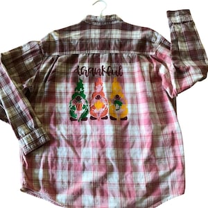 May include: A red and white plaid flannel shirt with the word "thankful" in cursive script and three gnome figures. The gnomes are green, orange, and yellow with fall-themed designs.
