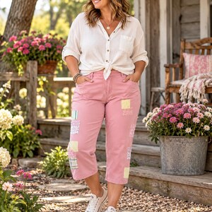 May include: A white long-sleeved button-down shirt with a front tie and pink cropped pants featuring various small, colorful fabric patches sewn onto the legs. The outfit is paired with white low-top canvas sneakers with laces.