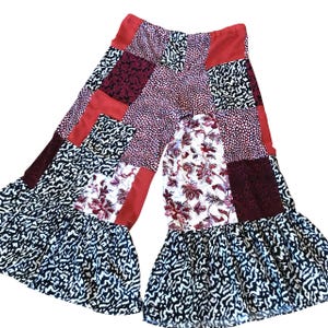 May include: Patchwork wide-leg pants with a red, white, and black color scheme. The pants have a ruffled hem and a loose fit.