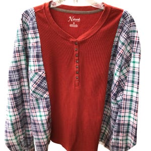May include: A long-sleeved shirt with a red waffle-knit body and plaid sleeves. The sleeves are a mix of navy, green, and white. The shirt has a V-neck and a button-up placket. The tag reads "Natural".