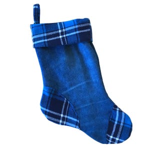 May include: A blue Christmas stocking with a denim texture. The cuff and toe feature a plaid pattern in shades of blue and white. A loop is attached for hanging.