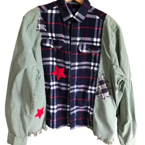 May include: A blue and red plaid flannel shirt with green striped sleeves. The shirt has red stars and a small tree design on the front. The sleeves are frayed at the edges.