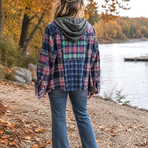 May include: A long-sleeve button-down shirt featuring a patchwork design of various plaid patterns in navy blue, pink, and green, with a dark gray attached hood and a frayed hemline, paired with blue denim jeans with a flared leg silhouette.