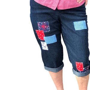 May include: Blue denim capri pants with red, white, and blue patchwork details. The patches feature stars, gingham, and fireworks.