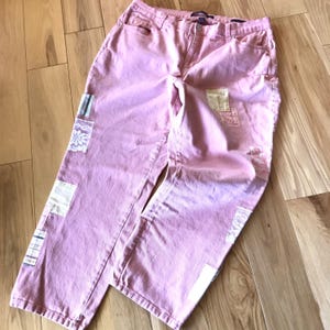 May include: Pink denim pants with patches of lace and fabric. The pants have a faded look and are distressed.
