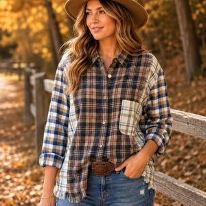 May include: A long-sleeve button-down shirt featuring a patchwork plaid pattern in shades of blue, brown, and cream. The shirt has a collar, a single chest pocket, and a frayed hemline. It is paired with blue denim jeans and a brown felt hat.