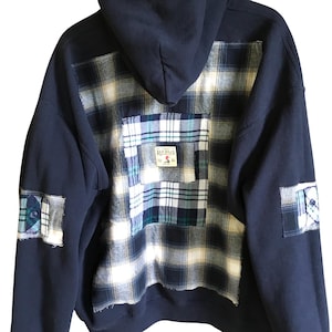May include: Navy blue hoodie with a plaid flannel back panel and patches. The plaid features white, blue, and green colors. The hoodie has a hood and a small patch that says "RED HEAD".