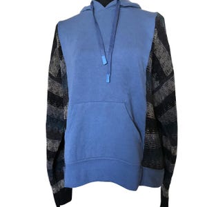 May include: A long-sleeve hooded sweatshirt featuring a solid light blue center panel with a matching drawstring hood and a front kangaroo pocket. The sleeves and side panels are constructed from a dark knit fabric with horizontal stripes.