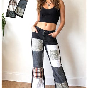 May include: Black denim pants featuring a patchwork design with various fabric squares in white, grey, and plaid patterns. The pants have a high-waisted fit, a button and zipper closure, and a wide-leg silhouette with visible stitching along the patches.