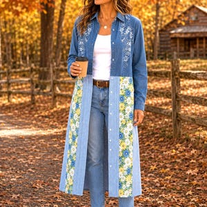 May include: A long-sleeved denim duster coat featuring white floral embroidery on the chest, a button-down front, and vertical panels of blue and white gingham fabric decorated with yellow and white daisy patterns, worn over a white top and jeans.
