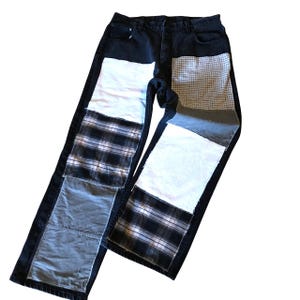 May include: Black denim jeans with patchwork details. Patches include white, plaid, and gray fabrics. The jeans have a classic five-pocket design and a straight leg fit.