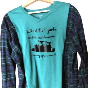 May include: A teal V-neck shirt with a plaid pattern on the sleeves. The shirt features the text "Lake of the Ozarks, Wishin and dreamin... Hurry up, summer!" and a graphic of a boat.