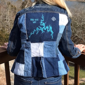 May include: A blue denim jacket with a patchwork design. The back of the jacket features a blue and turquoise embroidered map of Table Rock Lake.