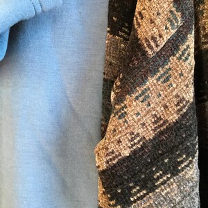 May include: A solid light blue garment layered beneath a textured fabric featuring a dark brown, black, and tan geometric pattern. The patterned fabric has a woven appearance with visible horizontal bands and a soft, slightly fuzzy surface texture.