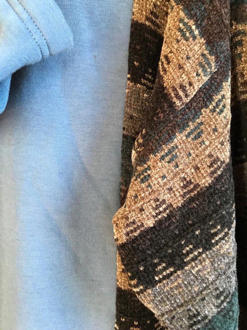 May include: A solid light blue garment layered beneath a textured fabric featuring a dark brown, black, and tan geometric pattern. The patterned fabric has a woven appearance with visible horizontal bands and a soft, slightly fuzzy surface texture.
